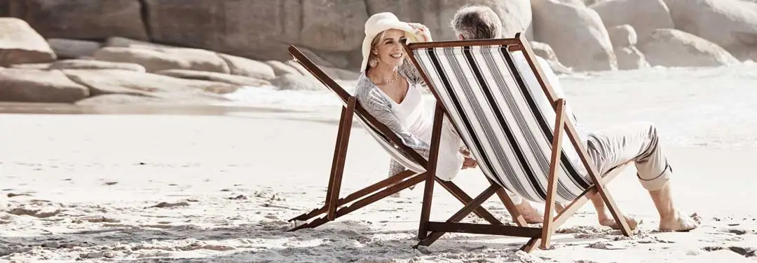 Two elderly people sitting on beach chairs on a beach on a sunny day.